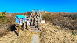 A wooden staircase leading to a beach area with a small blue structure and informational signs. - Cuckoo's Nest - 4 Bed, 2 Bath dog friendly home with pool, hot tub and tiki bar! (Southern Shores)