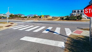 A crosswalk at an intersection with a stop sign, houses in the background, and a clear blue sky. - Cuckoo's Nest - 4 Bed, 2 Bath dog friendly home with pool, hot tub and tiki bar! (Southern Shores)