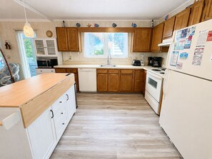 A kitchen with wooden cabinets, a white refrigerator, and a window providing natural light. - Cuckoo's Nest - 4 Bed, 2 Bath dog friendly home with pool, hot tub and tiki bar! (Southern Shores)