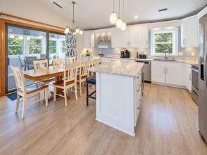 Une cuisine moderne avec des meubles blancs, un îlot central doté d’un plan de travail en marbre et un coin repas avec des chaises en bois.