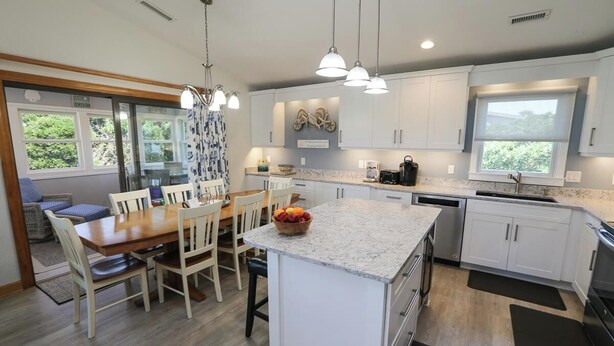 A modern kitchen with white cabinets, a granite countertop, and a dining area with wooden chairs and a table. - Sea Vista - Oceanside 6 Bed, 5.2 Bath, Rec Room, Pool, Hot tub! (Duck)