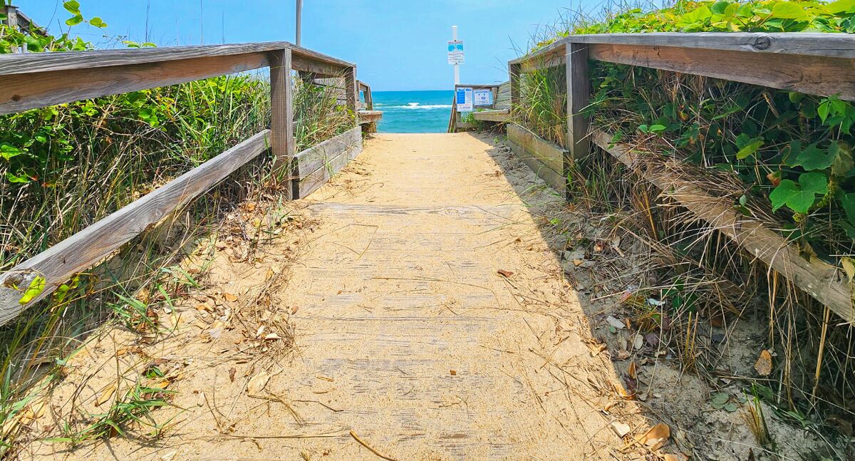 A sandy beach path with wooden railings leading to the ocean.