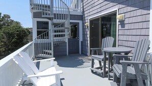A deck with white Adirondack chairs and a small table, a spiral staircase, and a sliding glass door leading to a covered area. - Sea Vista - Oceanside 6 Bed, 5.2 Bath, Rec Room, Pool, Hot tub! (Duck)