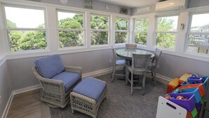 A room with a round table, wicker chairs, and a view of trees through large windows. - Sea Vista - Oceanside 6 Bed, 5.2 Bath, Rec Room, Pool, Hot tub! (Duck)