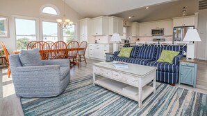 A spacious living room with a sofa, chairs, a coffee table, and a kitchen in the background. - SEAS THE VIEW Oceanside, close to Duck Village, 7 bed, 4.1 bath, pool, hot tub, dogs allowed! (Duck)