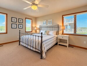 Une chambre à coucher comprenant un lit, des tables de chevet, un ventilateur de plafond et des œuvres d’art encadrées accrochées aux murs.