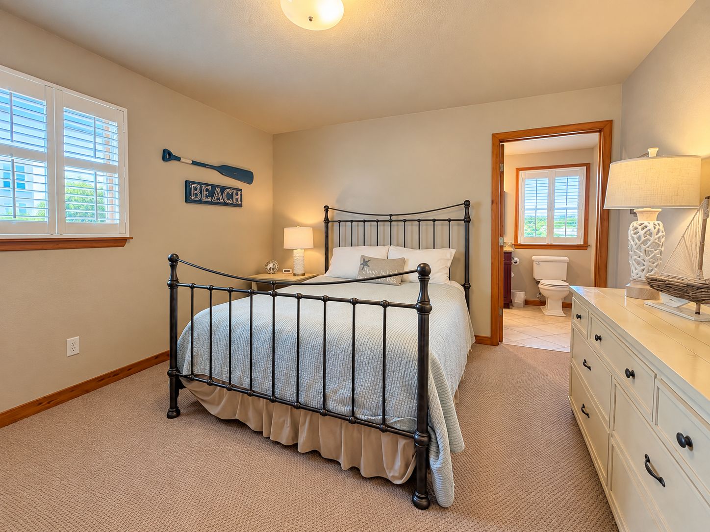 A bedroom with a bed, a nightstand, a dresser, a bathroom with a toilet, and a window with blinds.