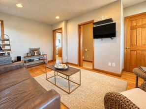 Un salon avec un canapé en cuir marron, une table basse et un téléviseur fixé au mur.