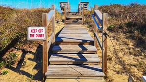 A wooden boardwalk leading to beach huts with a 'KEEP OFF THE DUNES' sign. - Serenity-Too - Oceanside Relaxation, 6 Bed, 4.1 Bath, pool, hot tub, dog friendly! (Southern Shores)