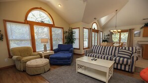 A spacious living room with a high ceiling, large windows, a dining area, and a kitchen. - Serenity-Too - Oceanside Relaxation, 6 Bed, 4.1 Bath, pool, hot tub, dog friendly! (Southern Shores)