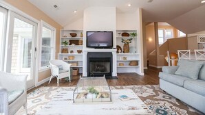 A living room with a fireplace, television, and shelves with decorative items. - Southern Comfort in Duck! Oceanside in Duck, 6 bed, 6.1 bath, dog friendly with pool and hot tub! (Duck)