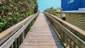 A wooden boardwalk leading to a building with a blue exterior. - Southern Comfort in Duck! Oceanside in Duck, 6 bed, 6.1 bath, dog friendly with pool and hot tub! (Duck)