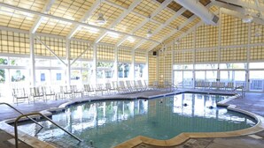 An indoor swimming pool with clear glass walls, sunlit ceiling, and multiple lounge chairs around the pool. - Southern Comfort in Duck! Oceanside in Duck, 6 bed, 6.1 bath, dog friendly with pool and hot tub! (Duck)
