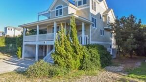 A two-story house with a covered porch and a small staircase leading to the entrance. - Southern Comfort in Duck! Oceanside in Duck, 6 bed, 6.1 bath, dog friendly with pool and hot tub! (Duck)