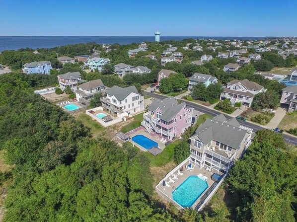 An aerial view of a residential area with houses, a lighthouse, and a large swimming pool. - Southern Comfort in Duck! Oceanside in Duck, 6 bed, 6.1 bath, dog friendly with pool and hot tub! (Duck)