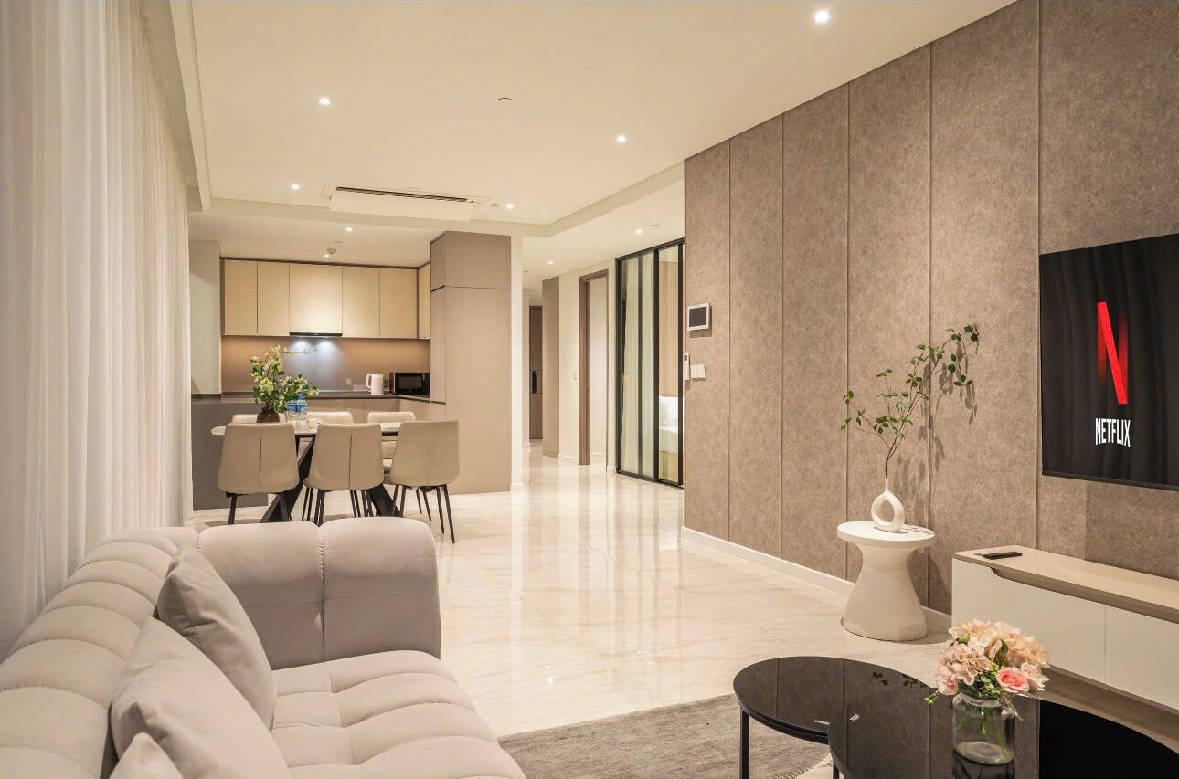 A modern living room with a sofa, a dining area, a kitchen, and a TV mounted on the wall.