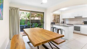 A modern kitchen with white cabinets, a central island, and a dining area with a wooden table and benches.