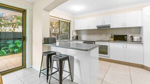 A modern kitchen with white cabinets, a central island with stools, and a view of a garden through a glass door.