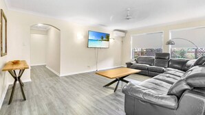 A spacious living room with a large sectional sofa, a wooden coffee table, and a flat-screen TV mounted on the wall.