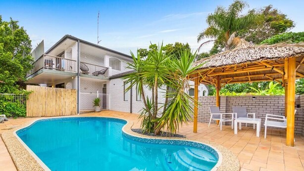 A modern house with a swimming pool, a covered patio, and a fenced garden area.