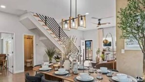 Zona pranzo moderna con tavolo in legno apparecchiato per quattro persone, una scala e una ventola a soffitto.