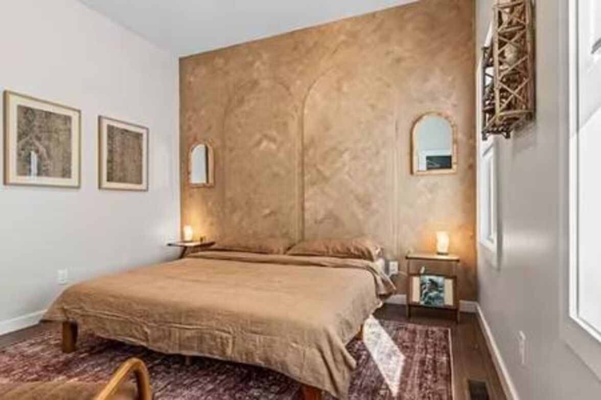 A bedroom with a large bed, two bedside tables, a wall-mounted mirror, and framed artwork on the wall.