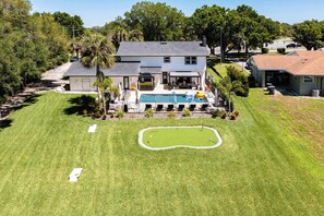 Uma casa de dois andares com piscina, varanda coberta e gramado bem cuidado.