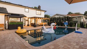 Un jardin avec une piscine, un cygne gonflable et un panier de basket.