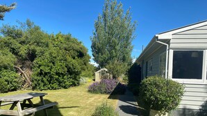 A residential property with a paved pathway leading to a wooden structure, surrounded by lush greenery and a picnic table. - Our Bach. Fish, ski or relax in an amazing alpine setting! (Lake Coleridge)