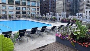 Ein Pool auf dem Dach mit Liegestühlen und Blumenkästen, umgeben von modernen Gebäuden.