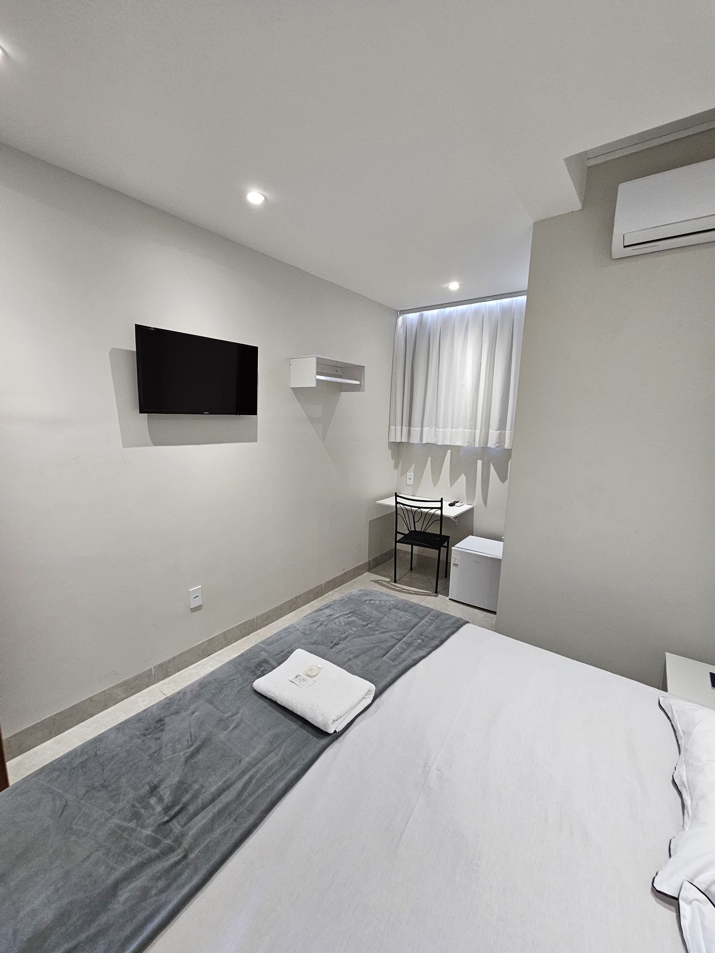 Una habitación de hotel moderna con una cama, un escritorio, una silla, un televisor y un equipo de aire acondicionado.