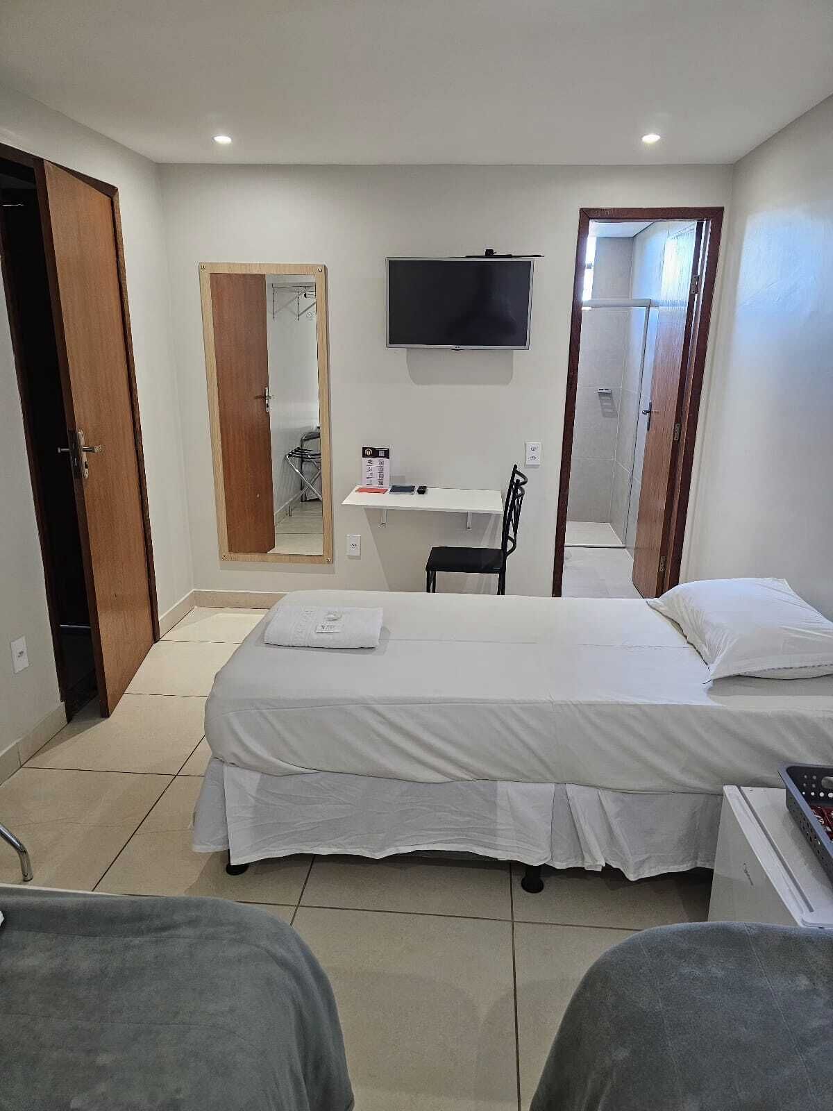 A hotel room with a large bed, a desk with a chair, a TV, and a shower area.