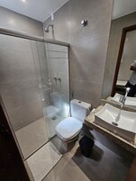 Un baño moderno con cabina de ducha acristalada, inodoro blanco y lavabo con encimera de granito.