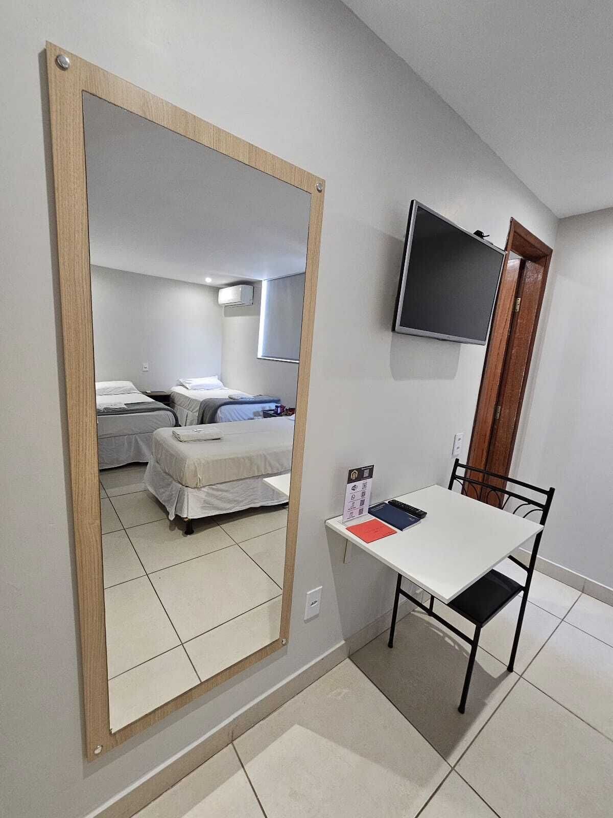 Habitación de hotel con un espejo grande, una cama, una mesita de noche con televisor y un escritorio pequeño con una silla.