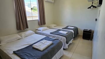 Quarto de hotel com três camas, ar-condicionado, ventilador de teto e janela com cortinas.