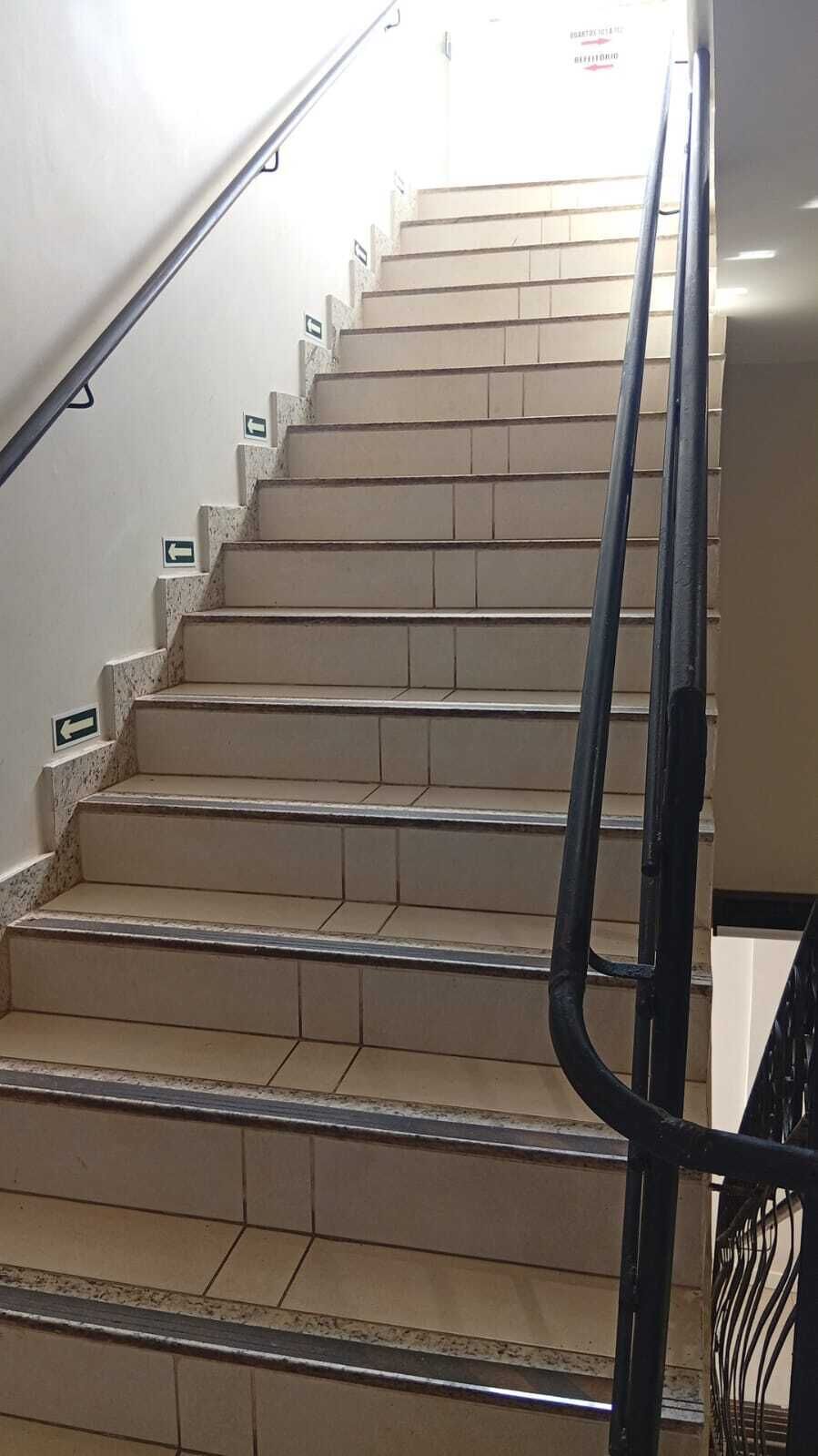 A staircase with beige tiles and black handrails, leading to an upper floor.