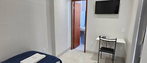 A bedroom with a bed, a desk, a chair, and a TV.