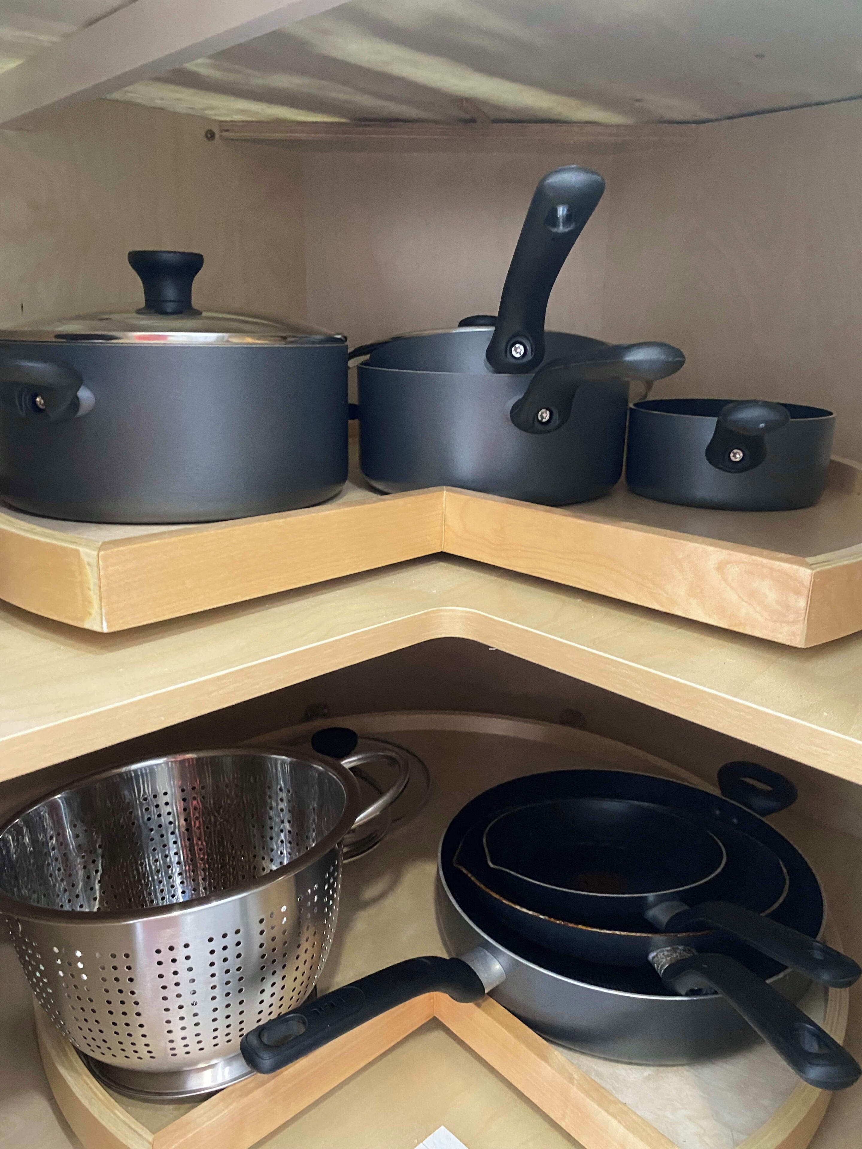 A kitchen with wooden shelves holding various cookware, including pots, pans, and a colander.