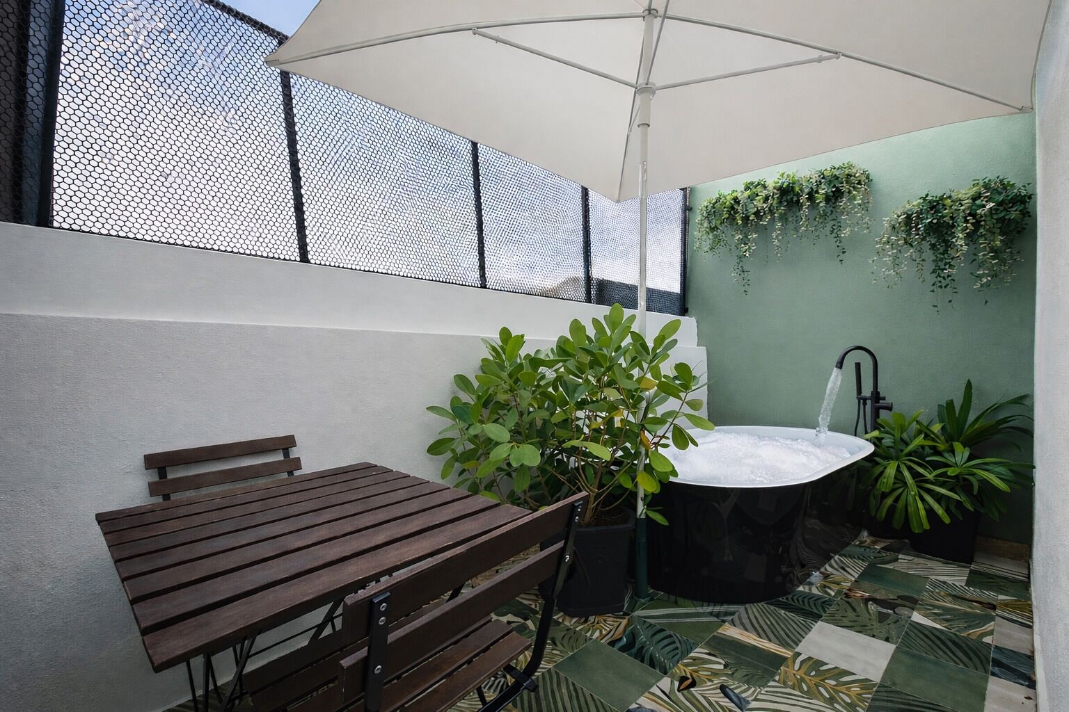 Un espace patio comprenant une table en bois, une plante en pot, une baignoire noire et un élément décoratif aquatique.
