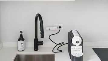 A kitchen with a white countertop, a black faucet, a coffee maker, and a shelf with dishes and glasses.