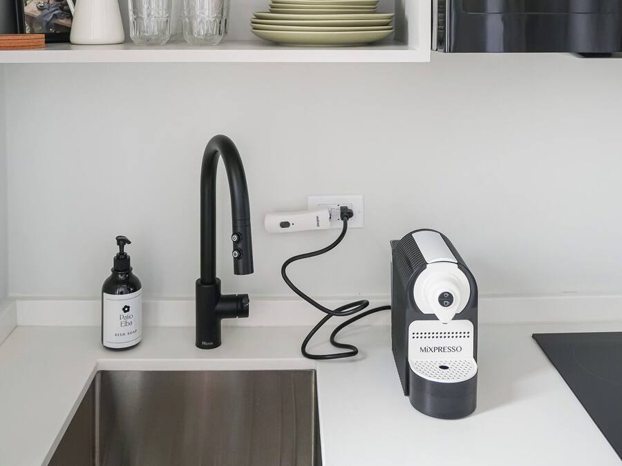 A kitchen with a white countertop, a black faucet, a coffee maker, and a shelf with dishes and glasses.