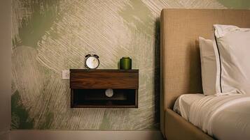 A bedroom with a bed, a nightstand with a clock and a green container, and a textured wall.