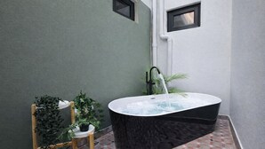 A spa area with a black freestanding bathtub, a small wooden stool, and a potted plant.