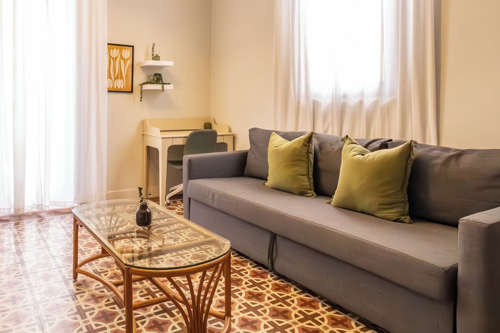 A modern living room with a grey sofa, two green cushions, a glass coffee table, and a patterned floor.