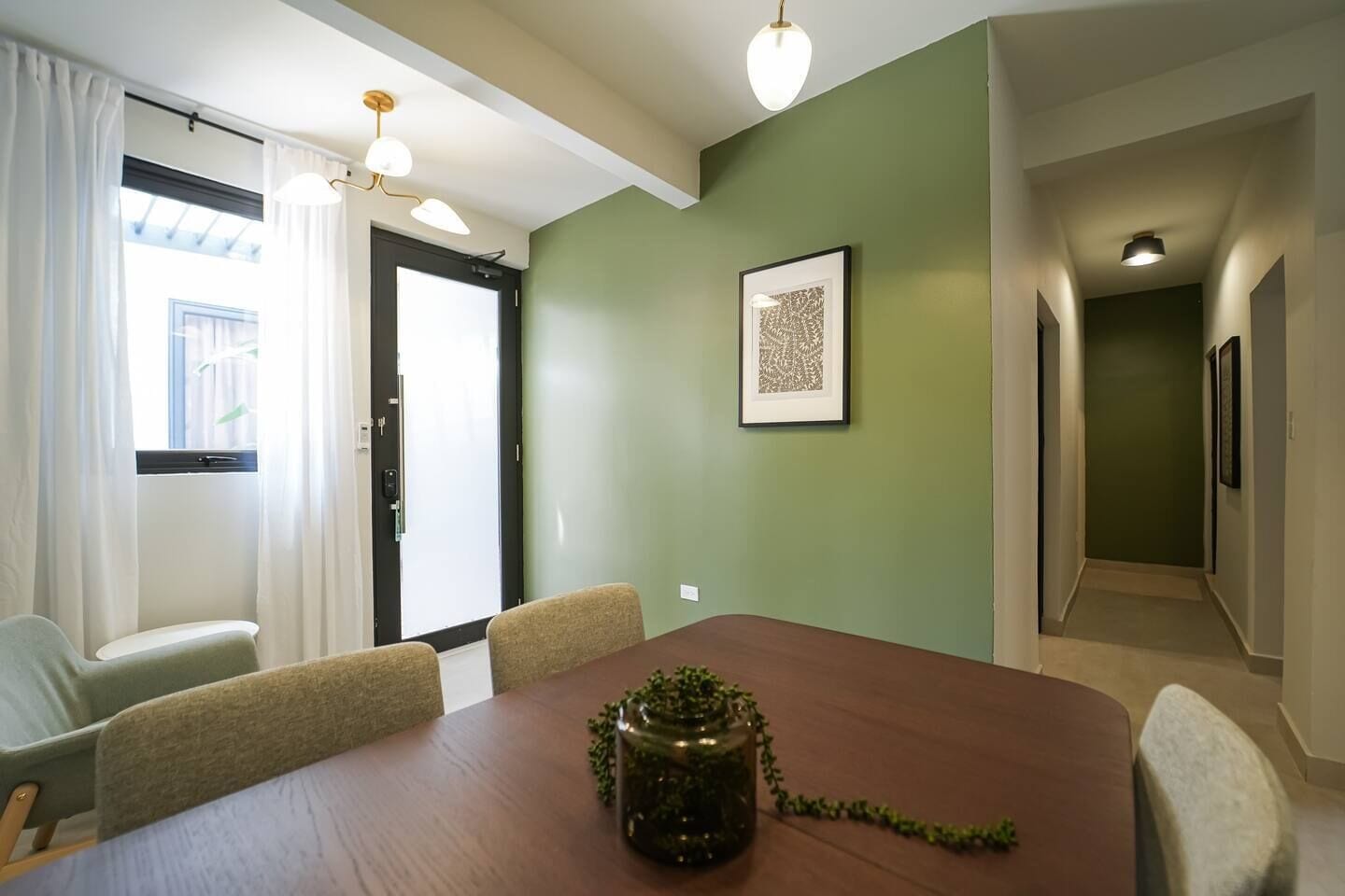 A conference room with a wooden table, four chairs, a potted plant, and a framed artwork on the wall.