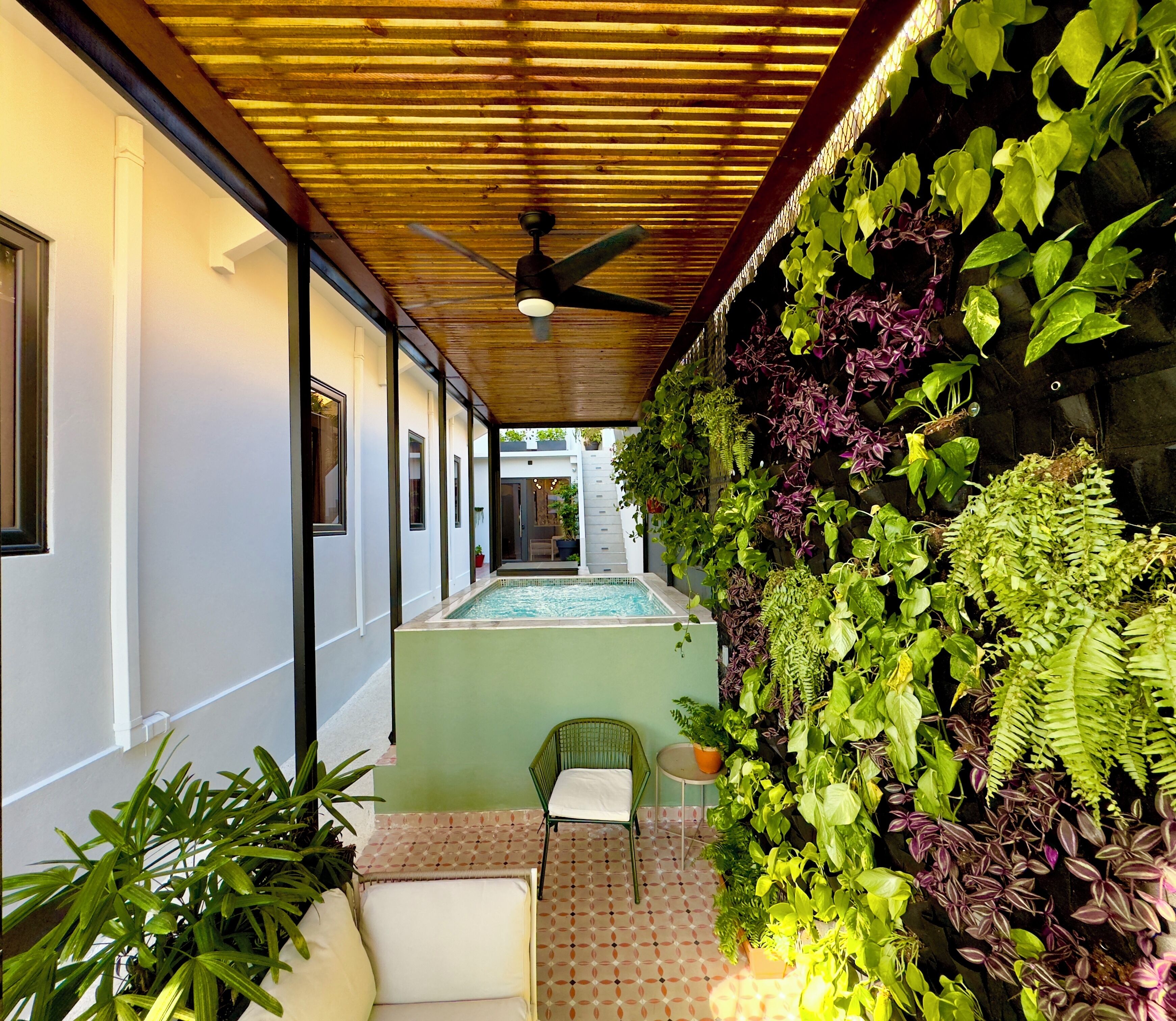 A covered outdoor area with a pool, a chair, and a variety of plants.