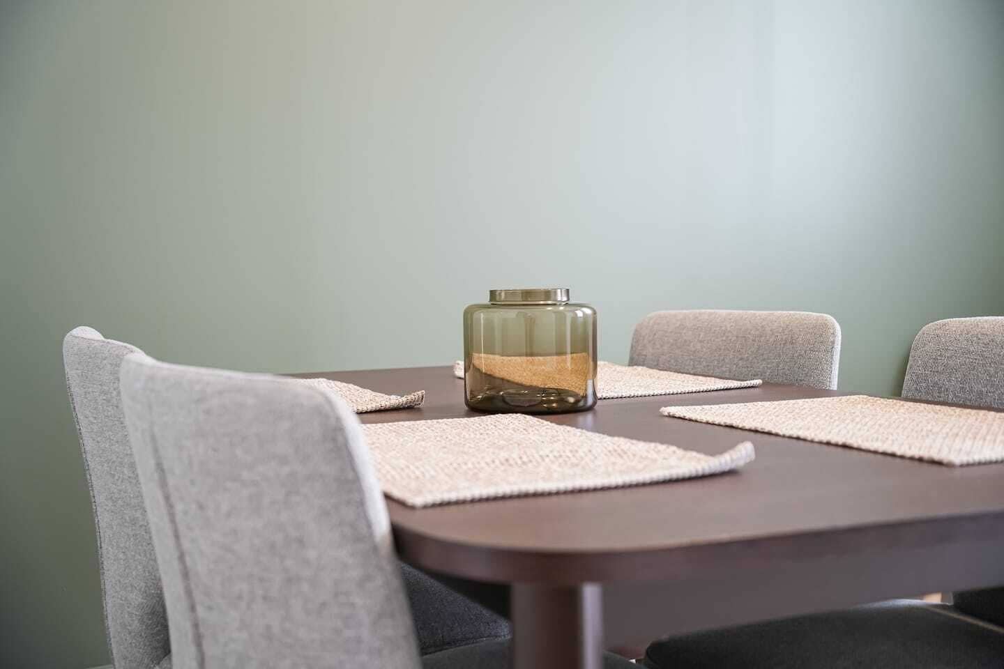 Una mesa de comedor con un florero de vidrio y posavasos.