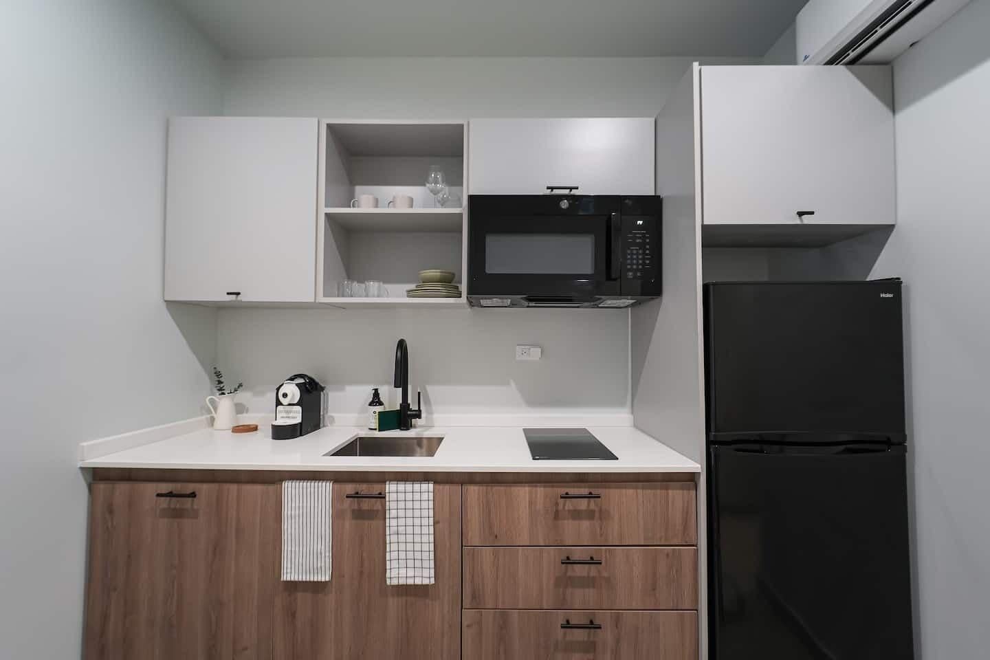 A modern kitchen with white cabinets, a black microwave, a black refrigerator, and a wooden countertop.