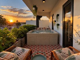 A rooftop terrace with a hot tub, seating area, and potted plants.