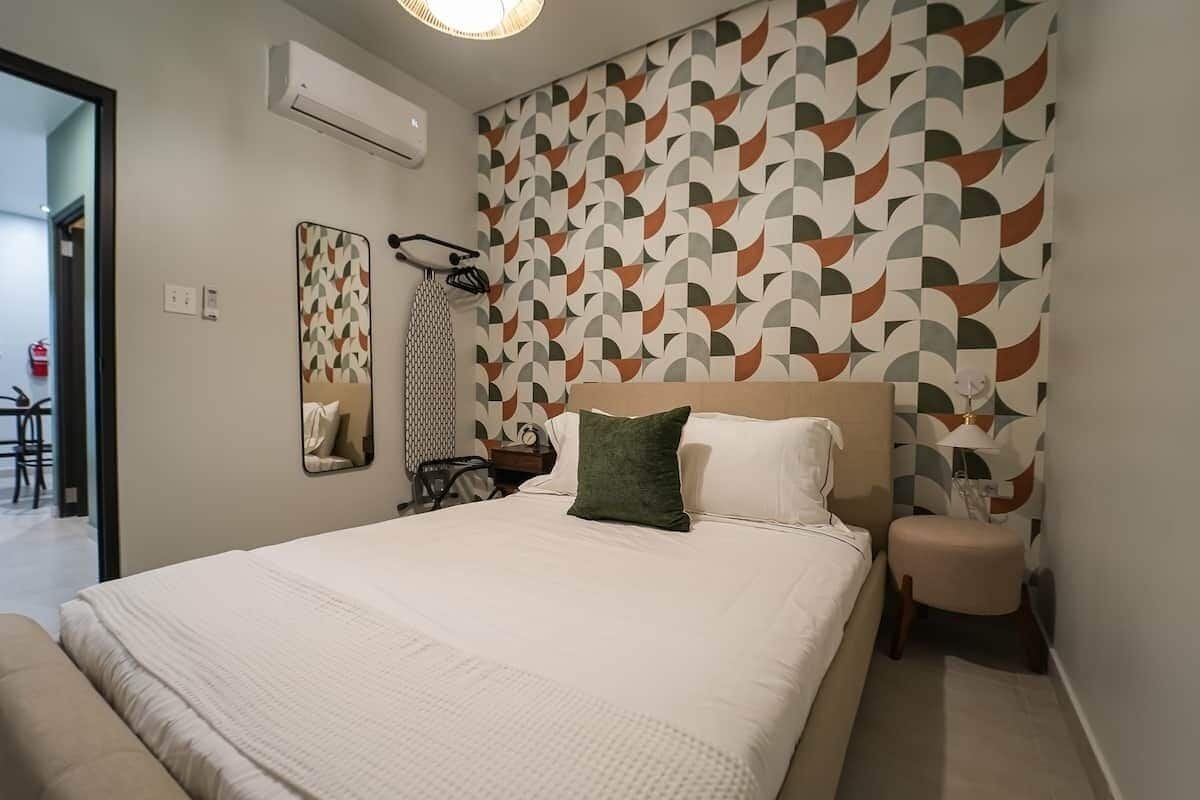 Habitación de hotel con una cama grande, una mesita de noche, un espejo y un papel tapiz estampado.